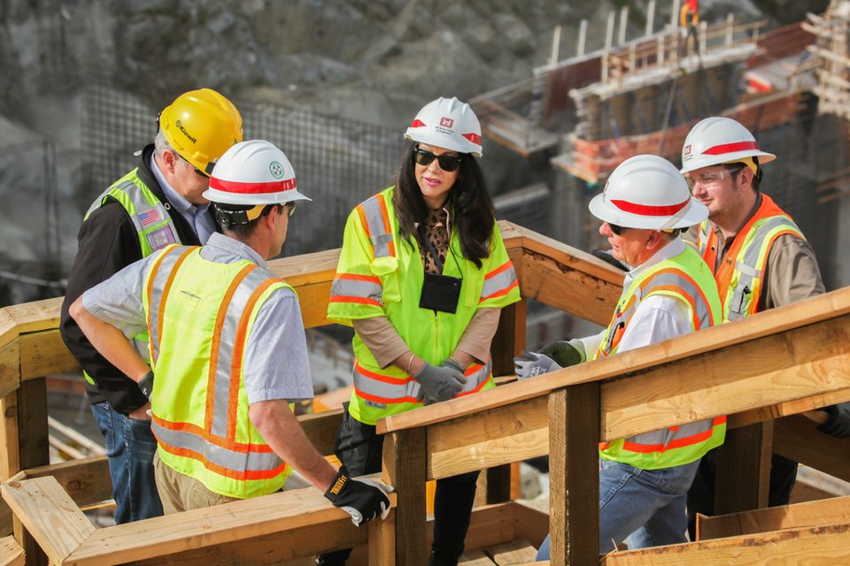 Five people in hard hats and hi-vis vests talking on a site