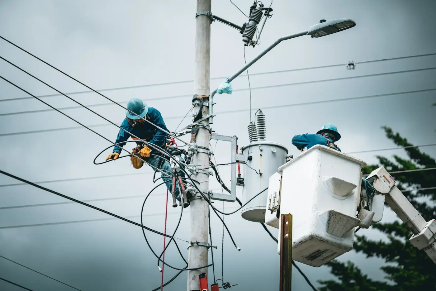 Two line workers in hard hats working from a bucket truck beside a power pole