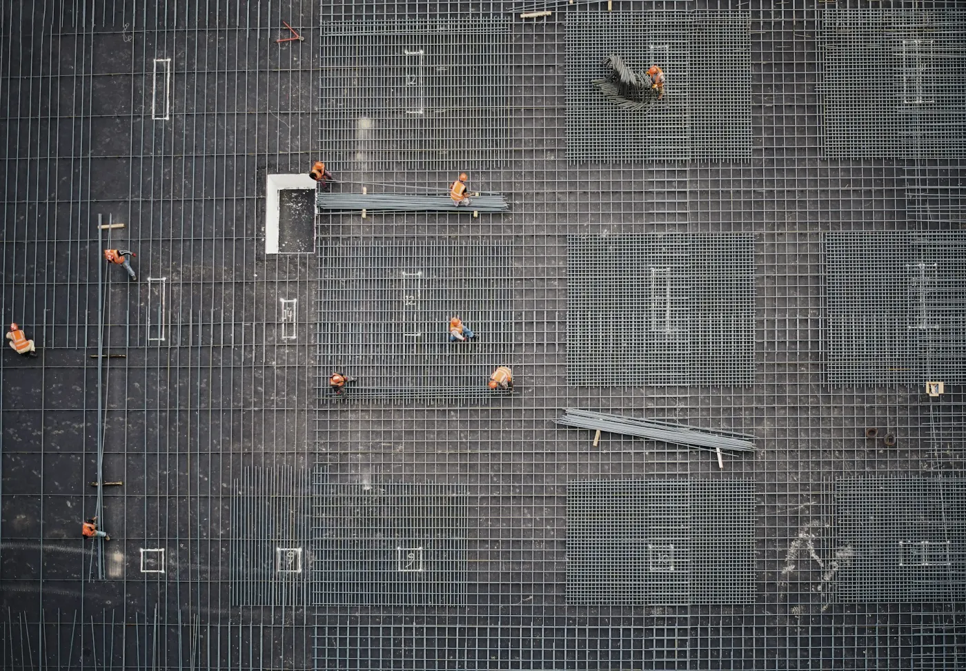 Workers spread across a grid of steel reinforcement, seen from above
