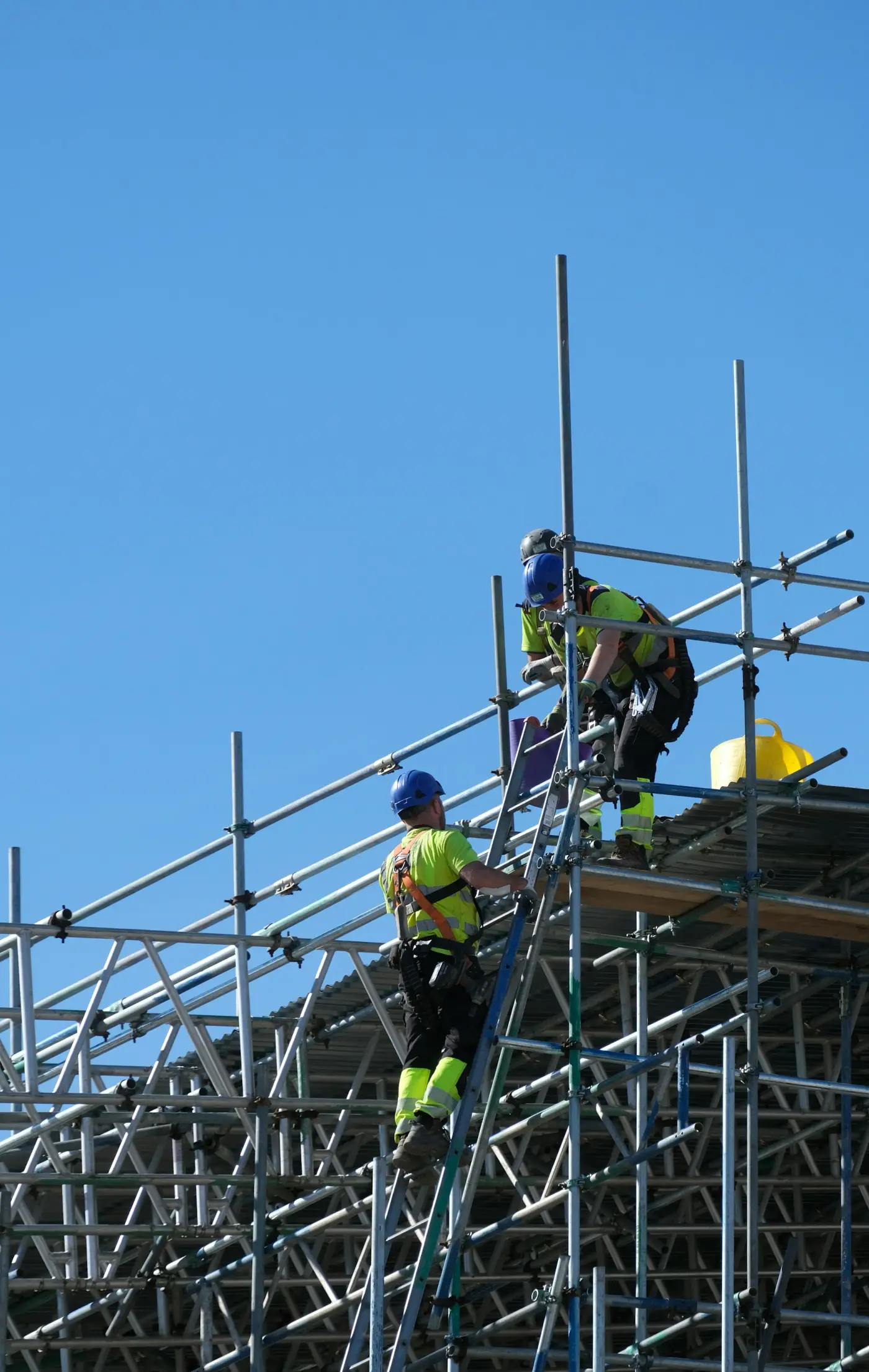 Two workers in hi-vis and hard hats climbing scaffolding