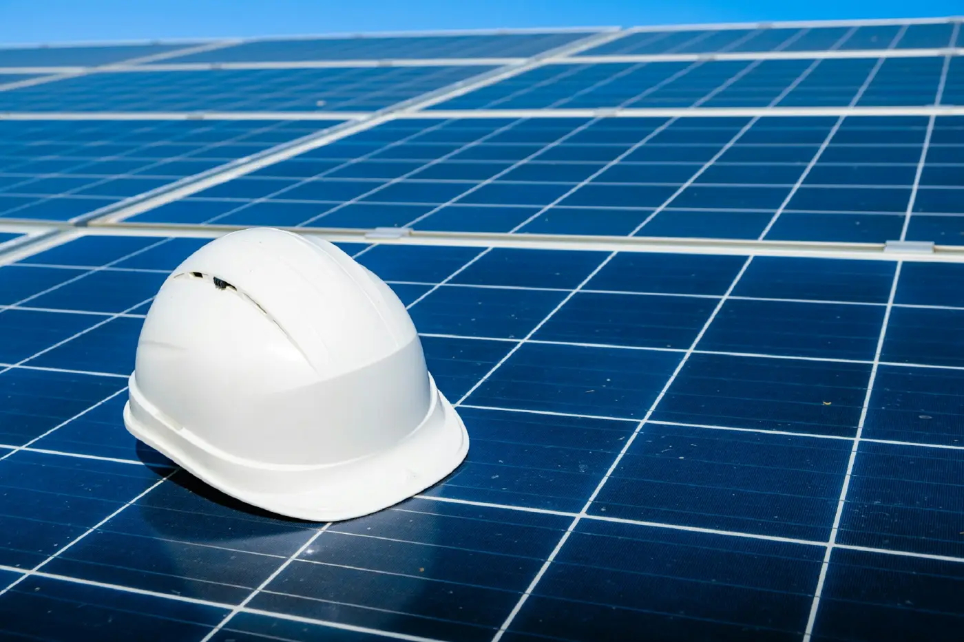 A worker in a hard hat beside rows of solar panels